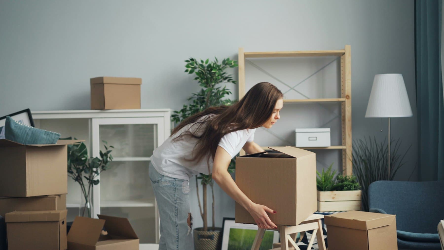 Person carrying a packed box through a living room during a move